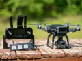 A drone with a 4K camera sits on a wooden table next to its controller and a spare battery, ready for its next follow drone adventure.
