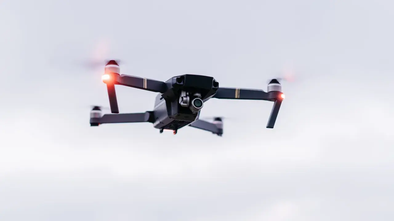 A drone hovers in the sky, its red lights blinking. Planning a trip? Be aware of Bahamas drone laws before you fly.