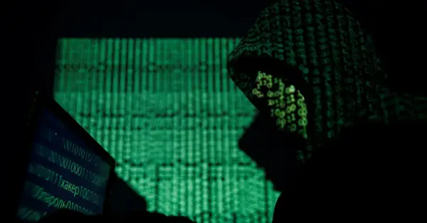 A hooded figure works on a laptop, bathed in the green glow of binary code. This scene evokes the shadowy world of China cyber espionage.